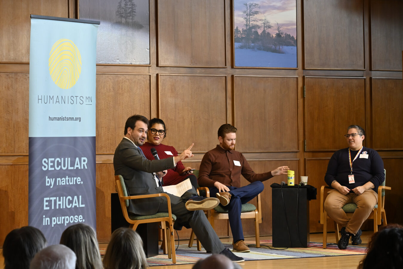 AHA Director Fish Stark facilitates a panel of speakers, all seated on a stage in a cathedral-like building